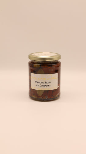 Ein Glas mit goldenem Deckel mit Conserve conti Pomodori Secchi alla Contadina - 270 g (sonnengetrocknete Tomaten in Öl) steht vor einem einfarbig beigen Hintergrund.