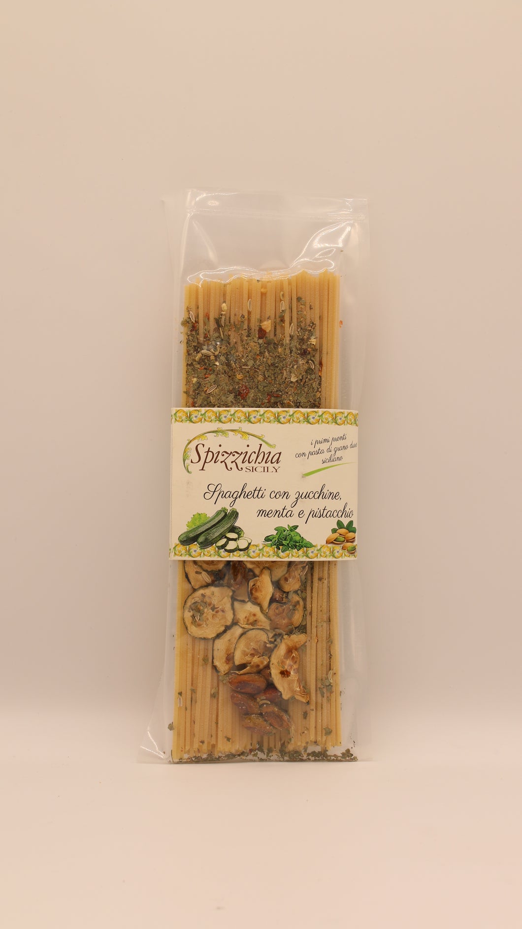 Eine durchsichtige Plastikverpackung mit Spizzicchia Spaghetti con zucchine, menta e pistacchio (200 g) mit getrockneten Zucchini, Minze und sizilianischen Pistazien. Auf dem Etikett steht der Produktname. Der Hintergrund ist einfarbig und hell.