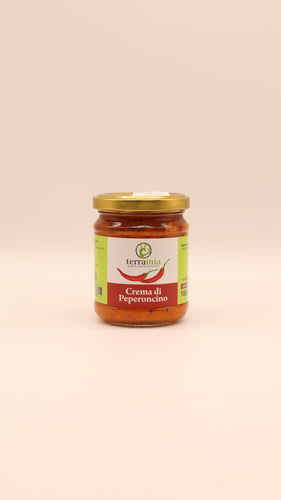 Ein Glas Terramia Patè di Peperoncino (180 g) mit goldenem Deckel, gefüllt mit roter Chilicreme, steht vor einem schlichten hellbeigen Hintergrund.