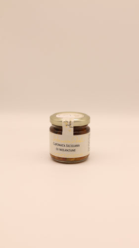 Ein 270-g-Glas mit Caponata siciliana di melanzane von Conserve Conti mit goldenem Deckel steht auf einem schlichten beigen Hintergrund. Diese sizilianische Antipasti ist eine stückige Gemüse-Auberginen-Mischung.