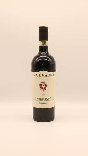Eine Flasche Salvano BARBERA ASTI SUPERIORE 2019 DOCG mit einem cremefarbenen Etikett mit goldenen Akzenten steht aufrecht vor einem schlichten hellen Hintergrund.