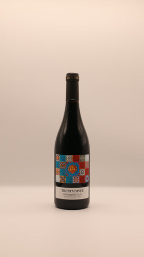 Eine Flasche TRENTACOSTE PRIMITIVO 2024 PUGLIA IGT 0,75 l von Giannis Enoteca mit einem farbenfrohen Mosaik-Etikett mit dekorativen Mustern vor einem schlichten hellen Hintergrund.