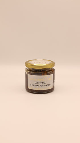 Ein Glas mit Conserve conti Confettura di cipolle e peperoncino - 190 g, mit goldenem Deckel und weißem Etikett mit goldener und schwarzer Schrift, steht vor einem schlichten hellbeigen Hintergrund.